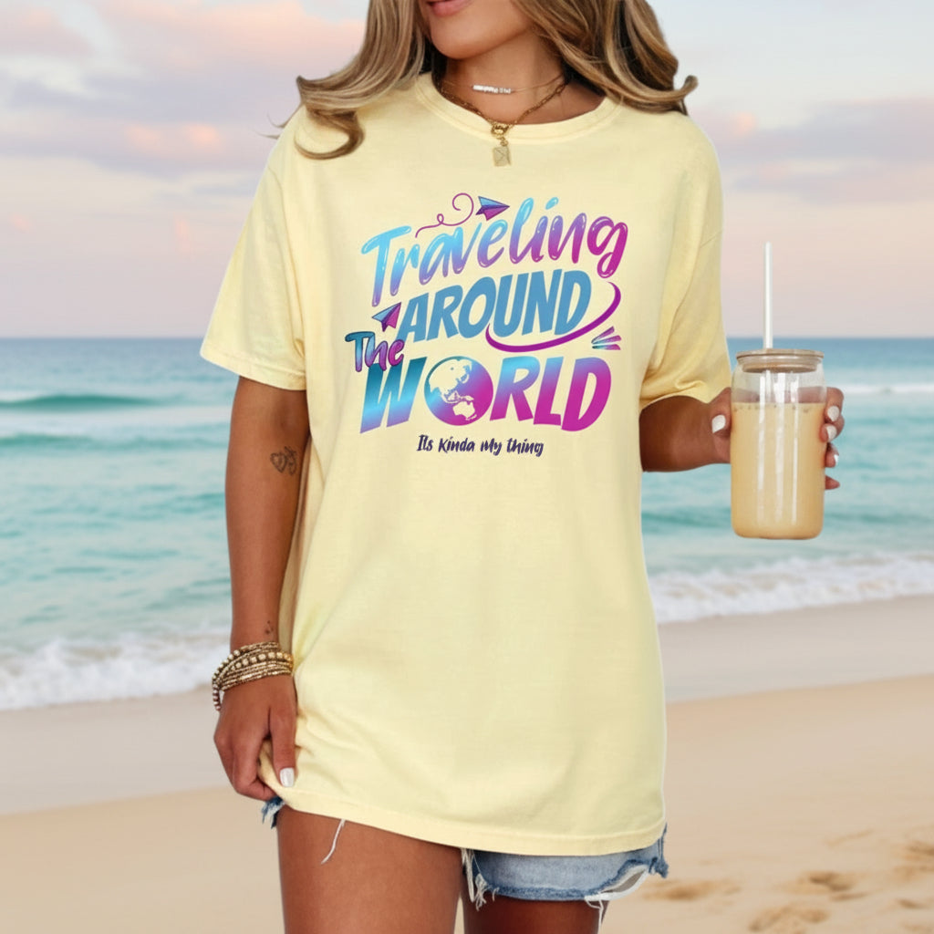 A person standing by the beach wearing a yellow t-shirt with the text 'Traveling Around The World' in a colorful, vintage-style font.