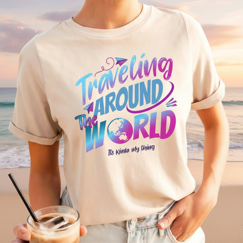 A woman wearing a tan T-shirt with the text 'Traveling Around the World' printed on it, standing by the beach.