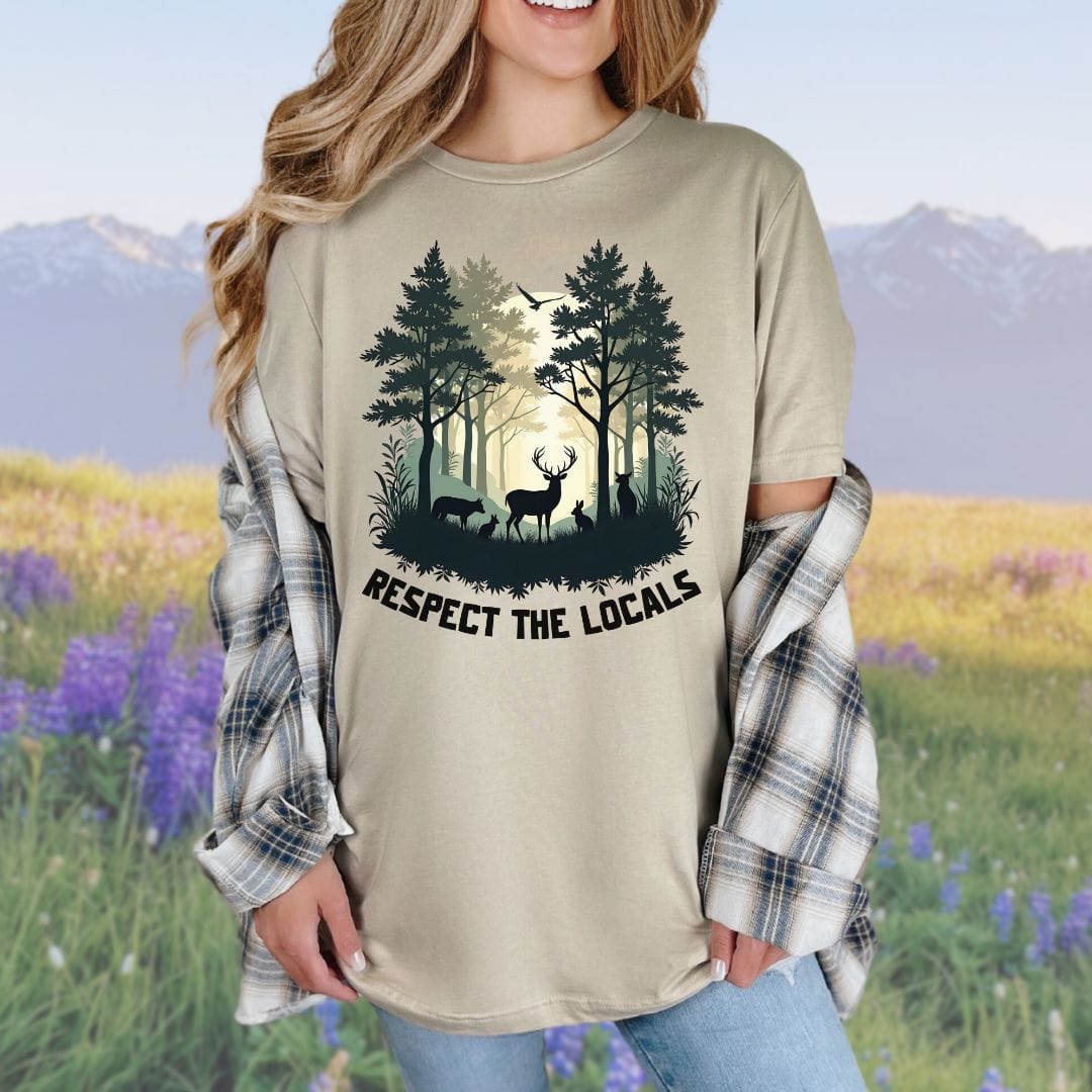 A person wearing a tan t-shirt with a graphic of a forest and deer and the text 'RESPECT THE LOCALS'.