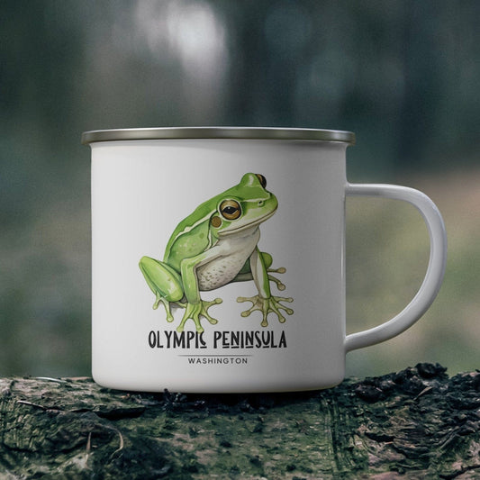 White mug with a green frog illustration and text on a wooden surface with a forest background