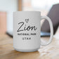 White mug with 'Zion National Park Utah' text on a wooden surface