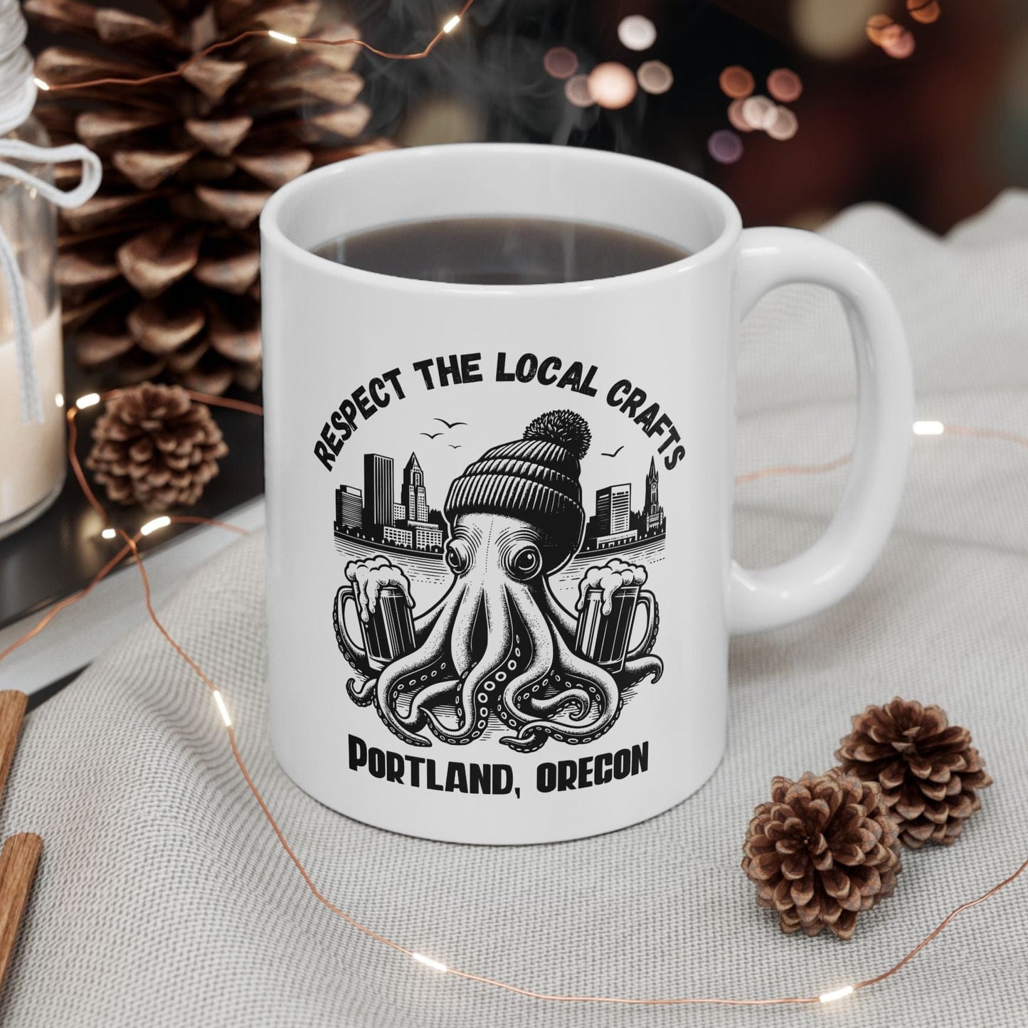 White mug with a black and white design featuring an octopus and text, placed on a table with decorative items.
