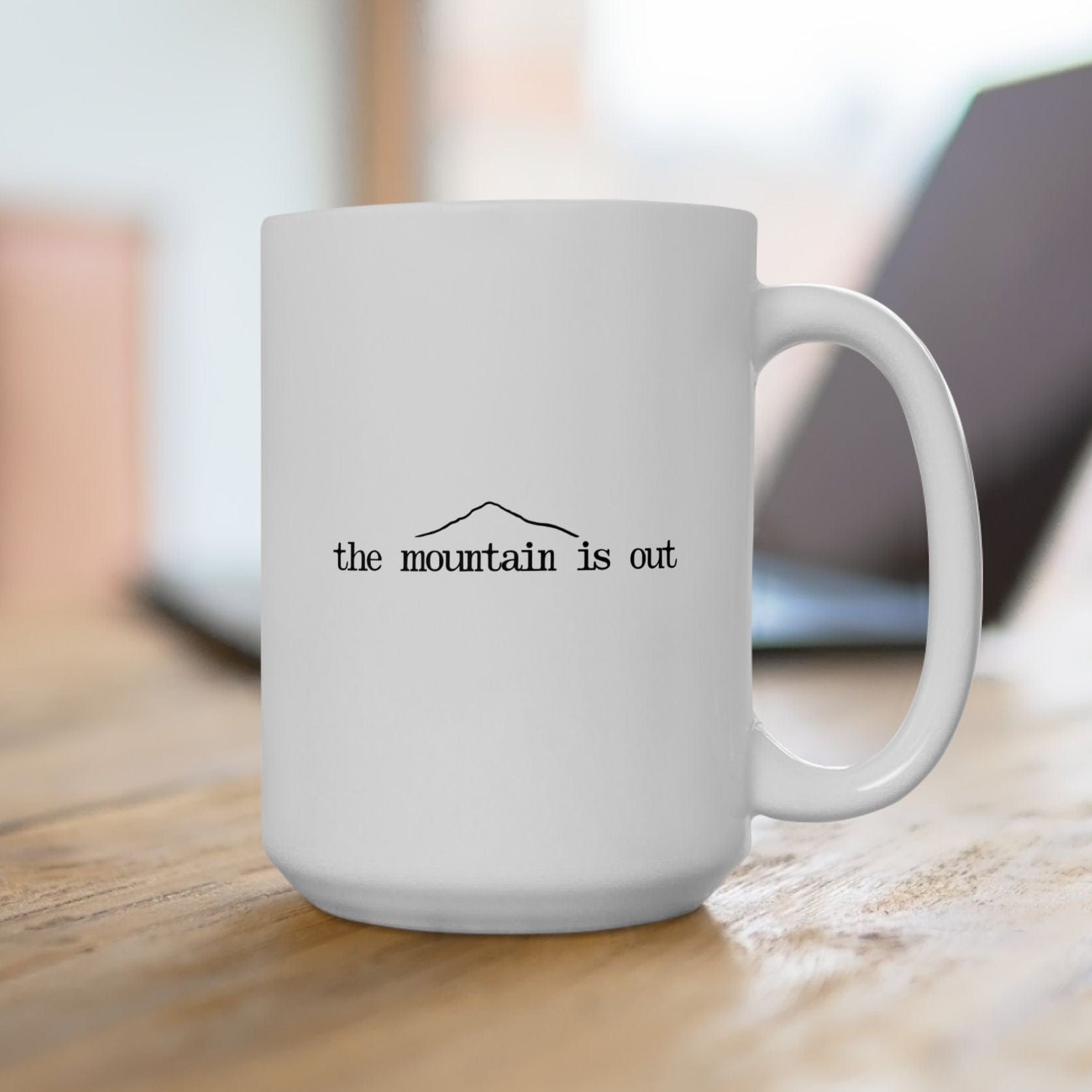 White mug with 'the mountain is out' text on a wooden surface