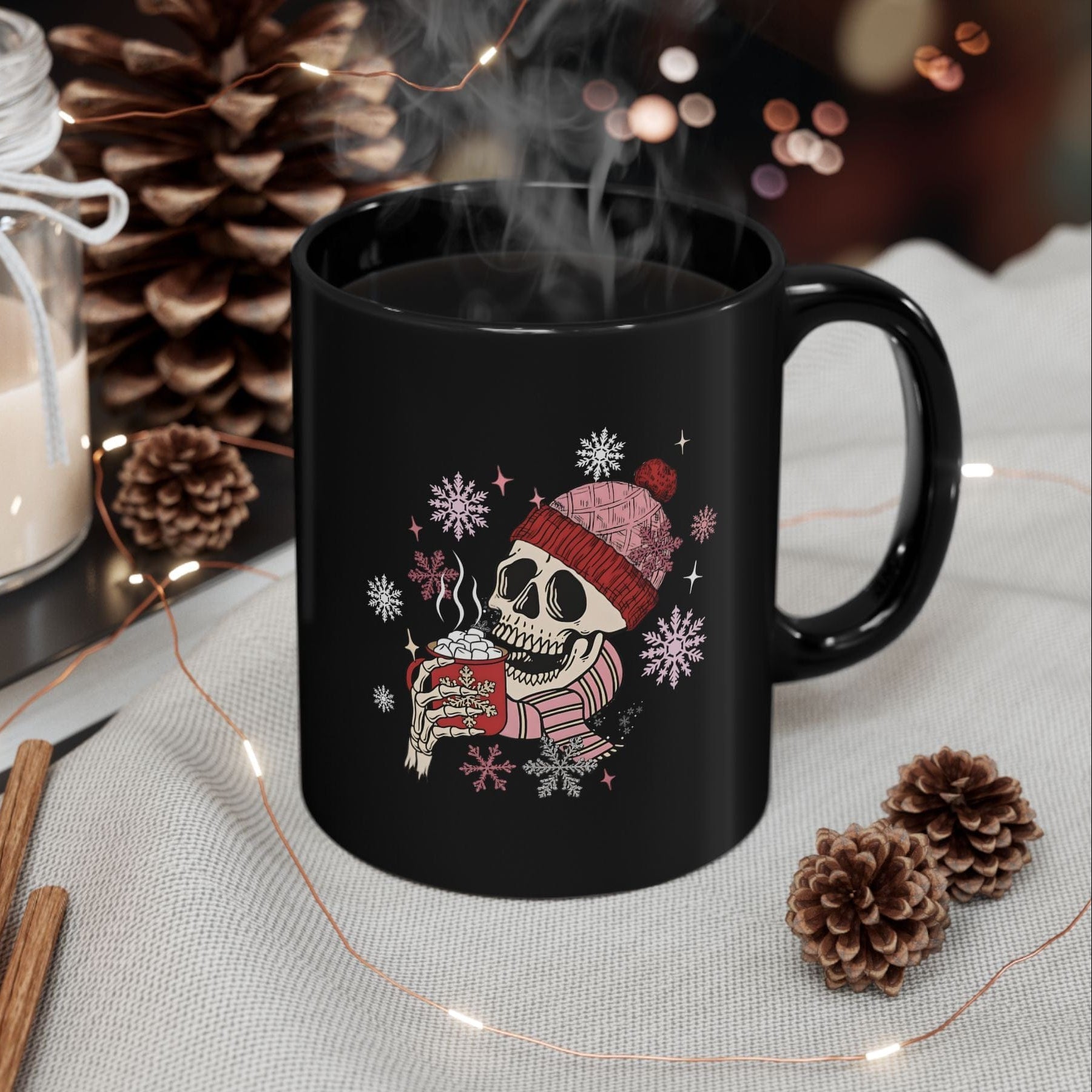 Black mug with a skeleton wearing a Santa hat and holding a cup, surrounded by decorative items on a table.