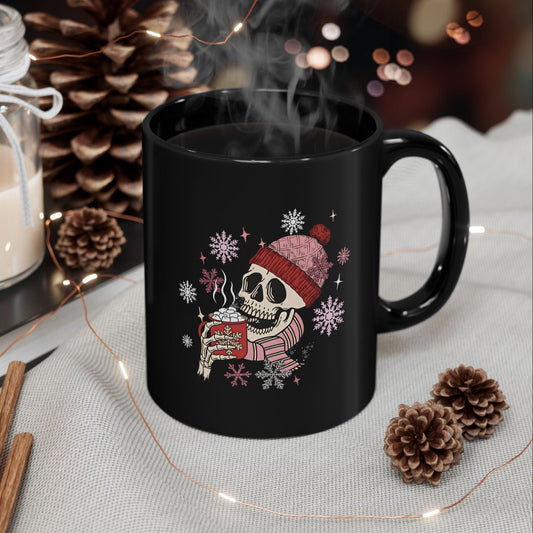 Black mug with a skeleton wearing a Santa hat and holding a cup, surrounded by decorative items on a table.