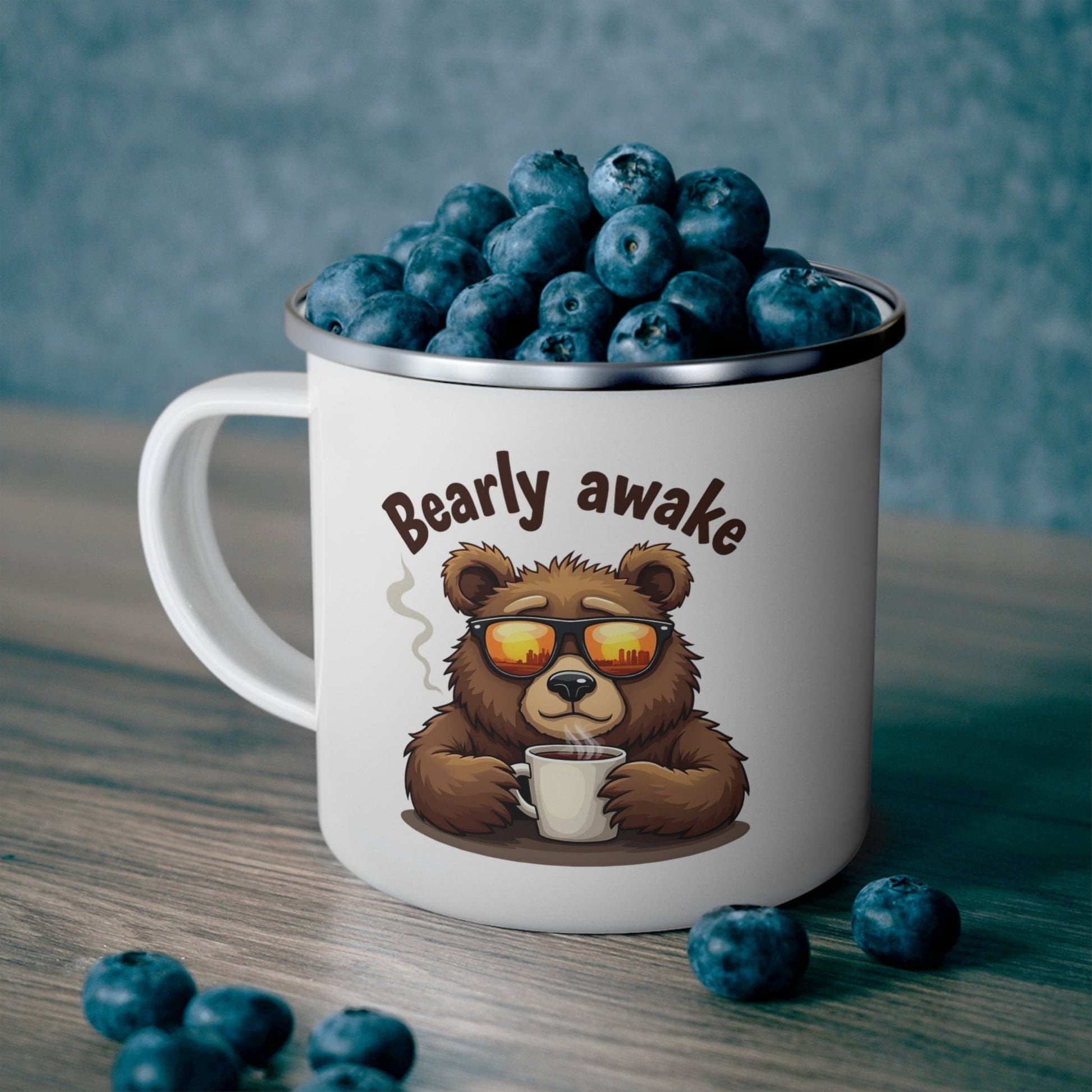 White mug with a bear illustration and 'Bearly awake' text, filled with blueberries on a wooden surface.