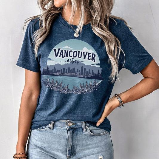 A woman wearing a heather navy blue graphic t-shirt with a 'Vancouver Vibes' cityscape print, paired with light-wash denim jeans.