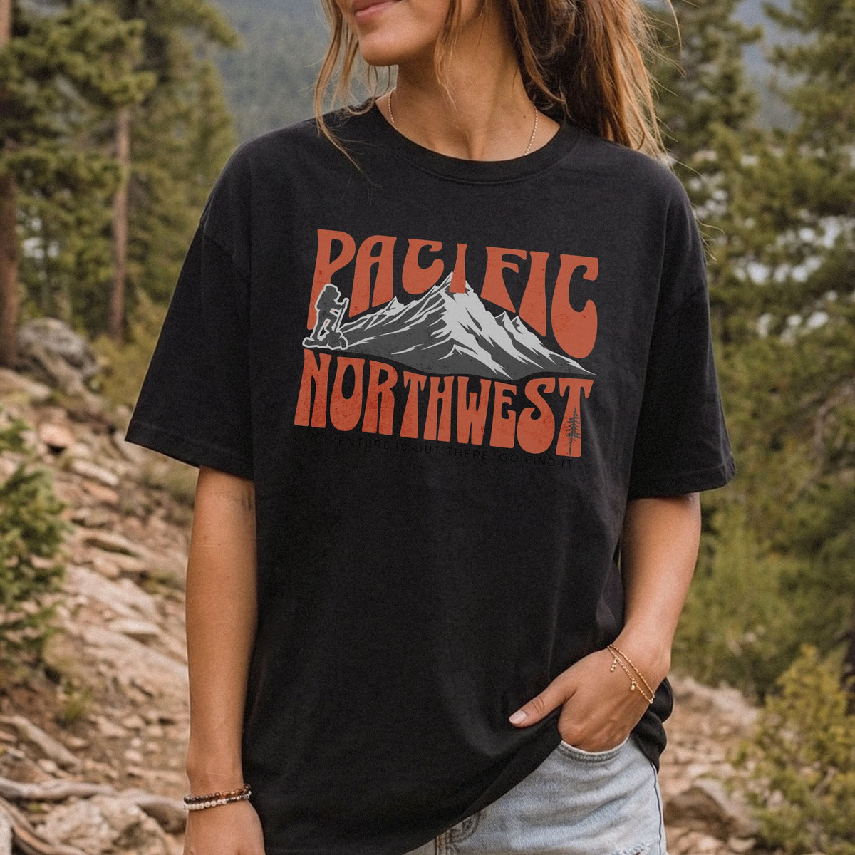A woman wearing a Pacific Northwest mountain hiking T-shirt with vintage orange graphic on a black garment-dyed tee.
