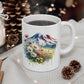 White mug with a mountain and flower design on a table with candles and pinecones.