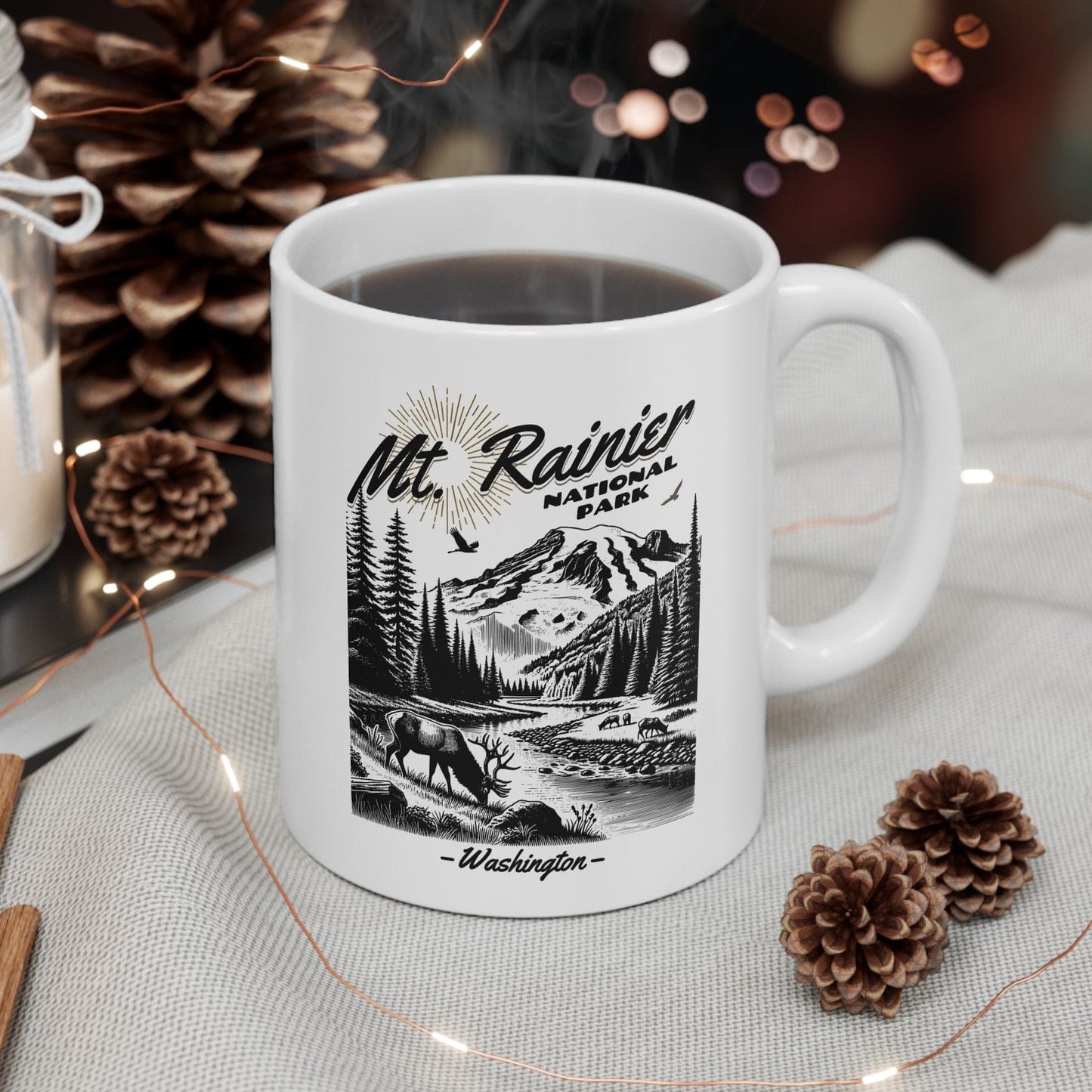 White mug with 'Mt. Rainier National Park' design on a table with decorative items.