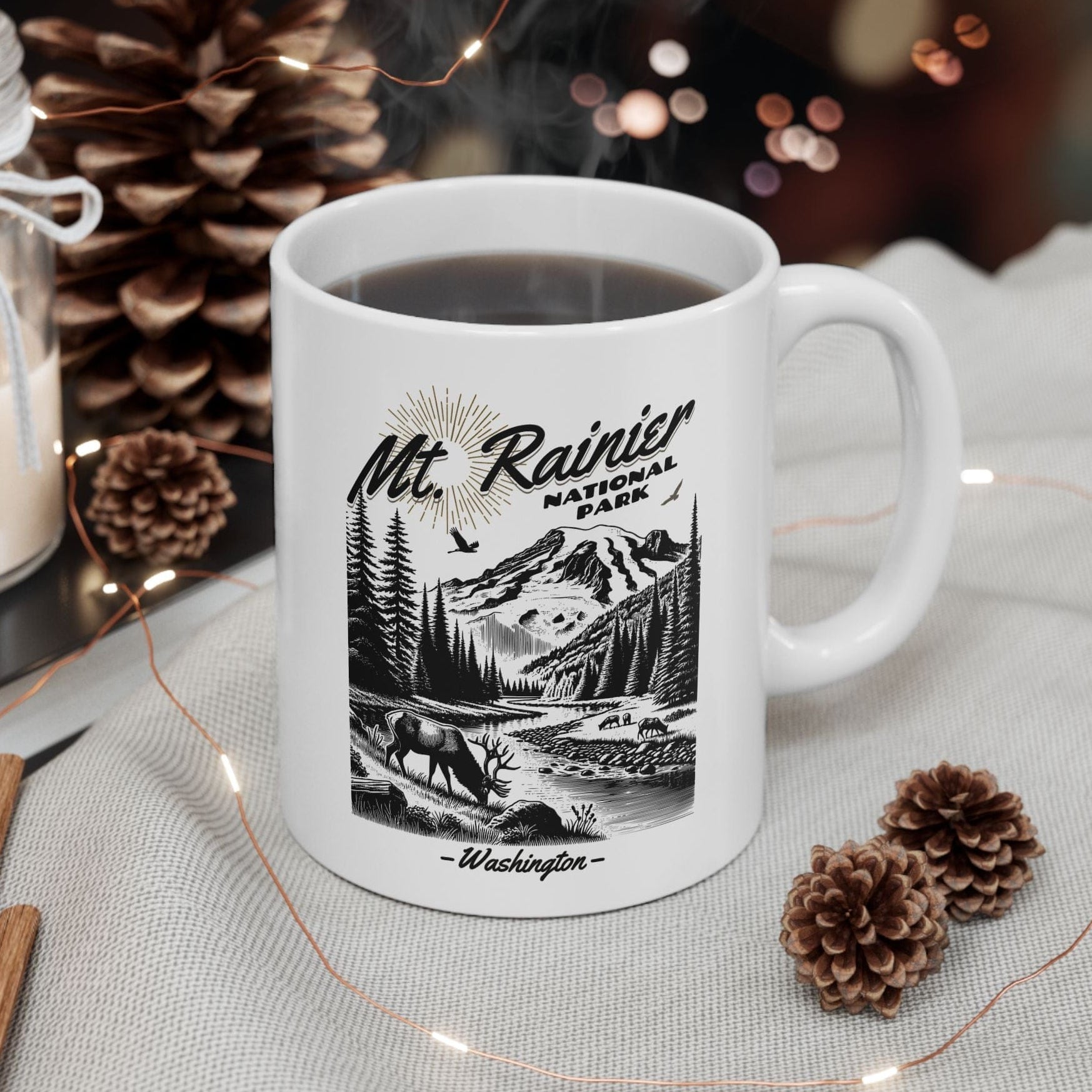 White mug with 'Mt. Rainier National Park' design on a table with decorative items.