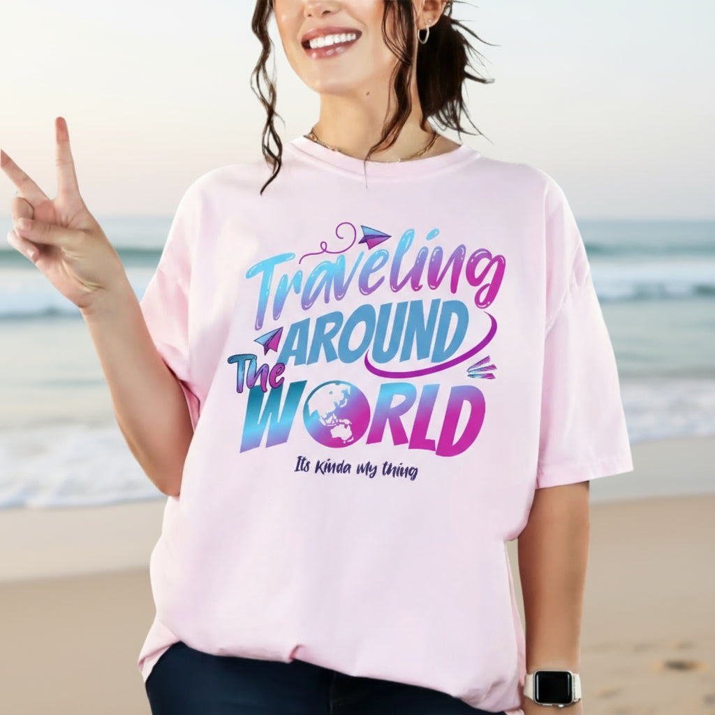 Person wearing a pink t-shirt with 'Traveling Around The World' text on a beach