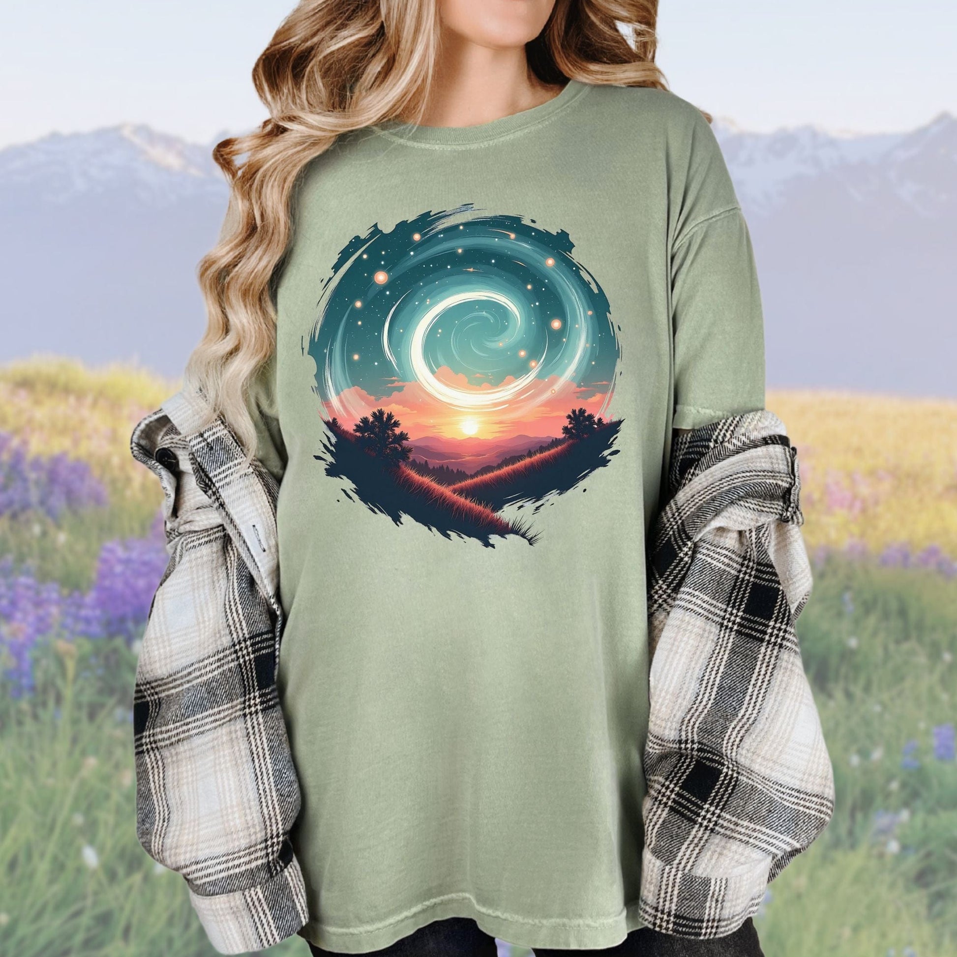 A person wearing a vintage-style graphic tee in a green color with a swirl pattern in the design, standing in a field with mountains in the background.