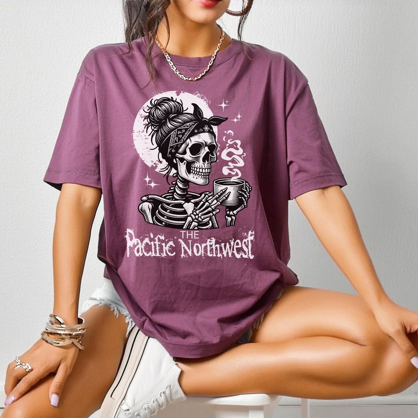 A person wearing a berry colored vintage-style tee with a graphic of a skull holding a mug and the text 'PACIFIC NORTHWEST'.