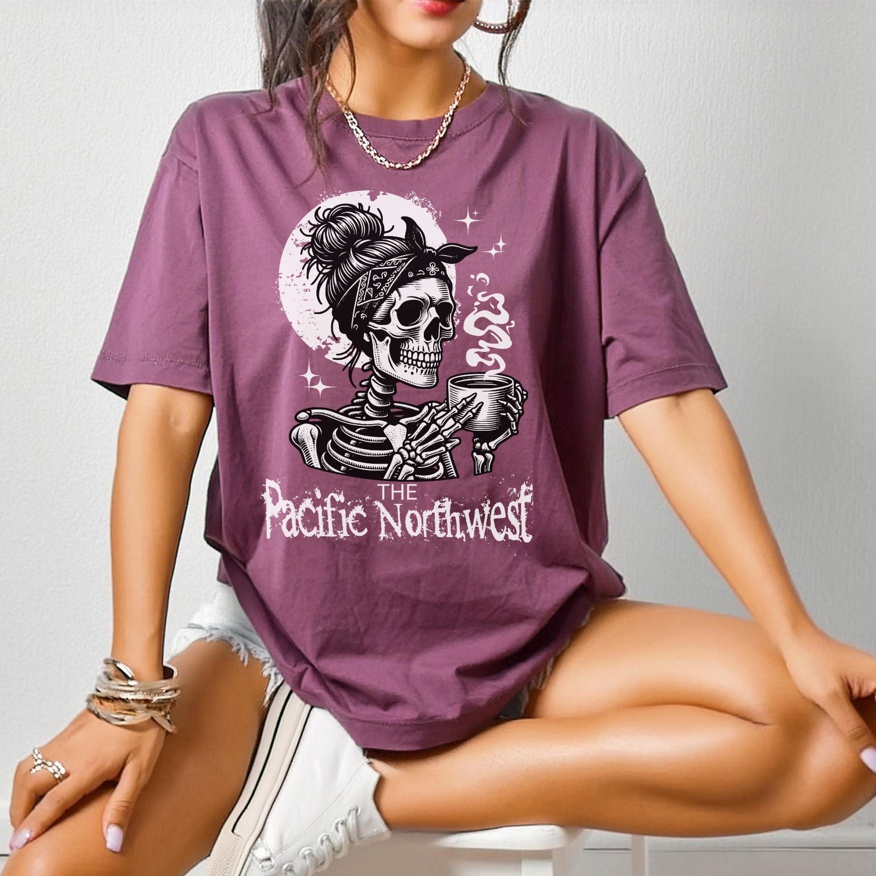 A person wearing a berry colored vintage-style tee with a graphic of a skull holding a mug and the text 'PACIFIC NORTHWEST'.