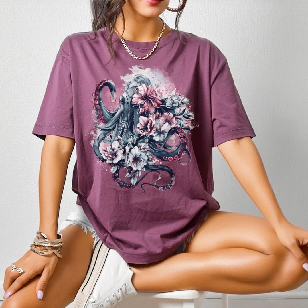 A person wearing a berry colored t-shirt with a vintage floral Kraken design.