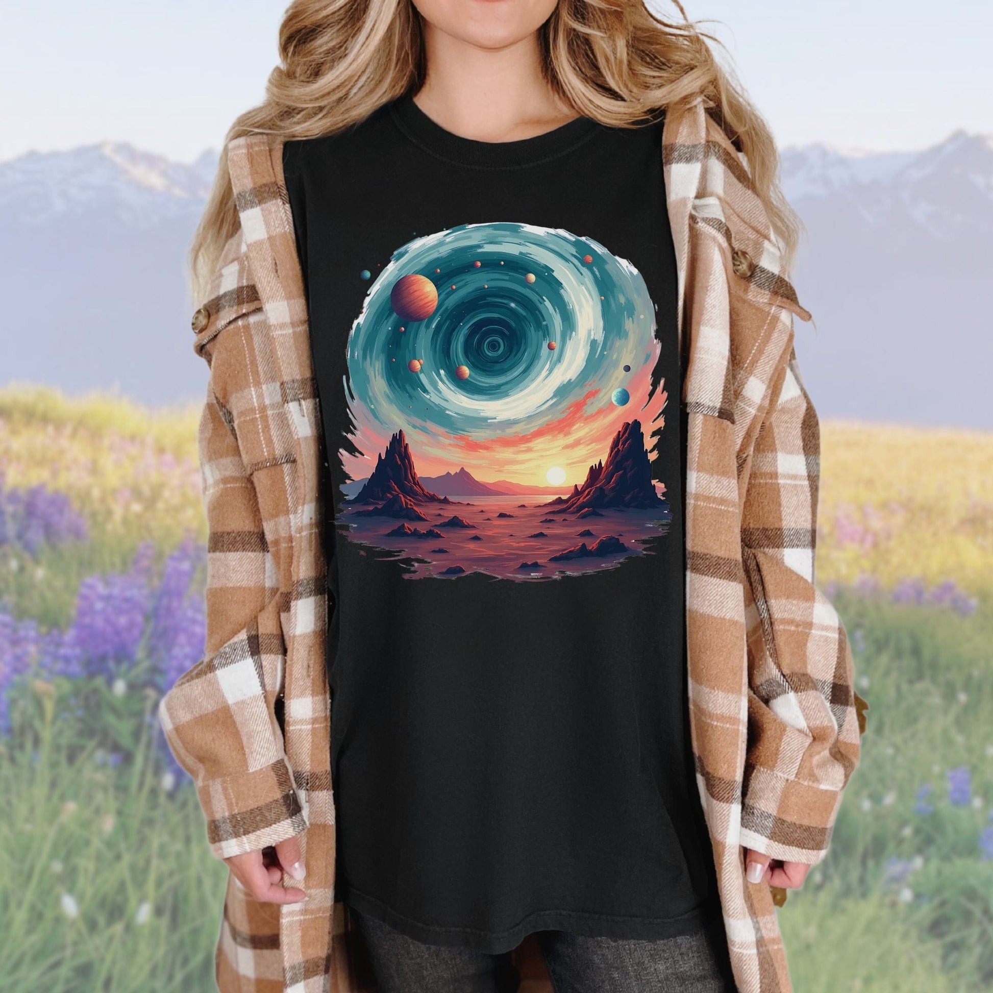 A person wearing a black t-shirt with a vintage cosmic swirls graphic, paired with a plaid shirt.