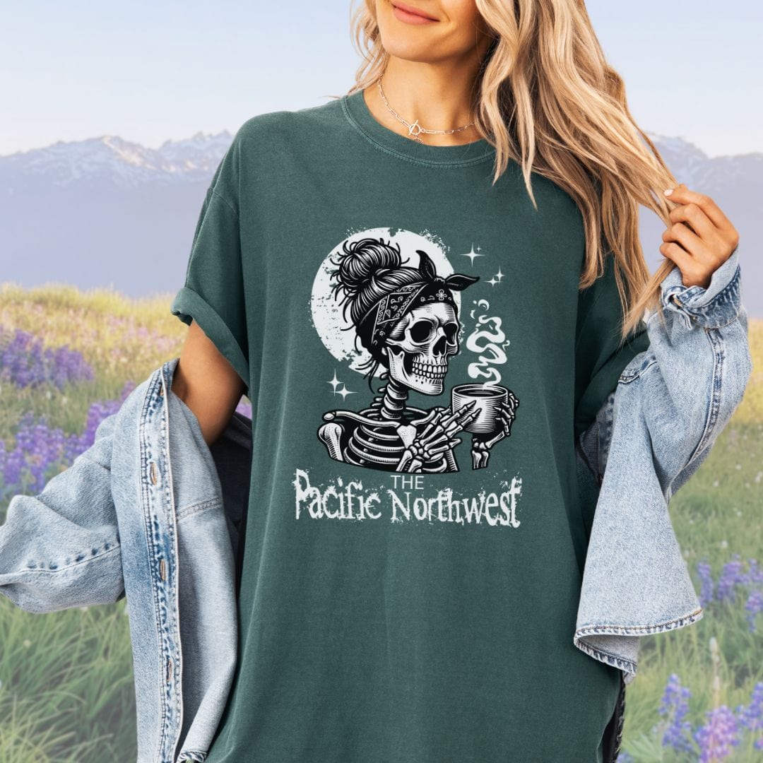 A person wearing a blue green vintage-style tee with a graphic of a skull holding a mug and the text 'PACIFIC NORTHWEST'.