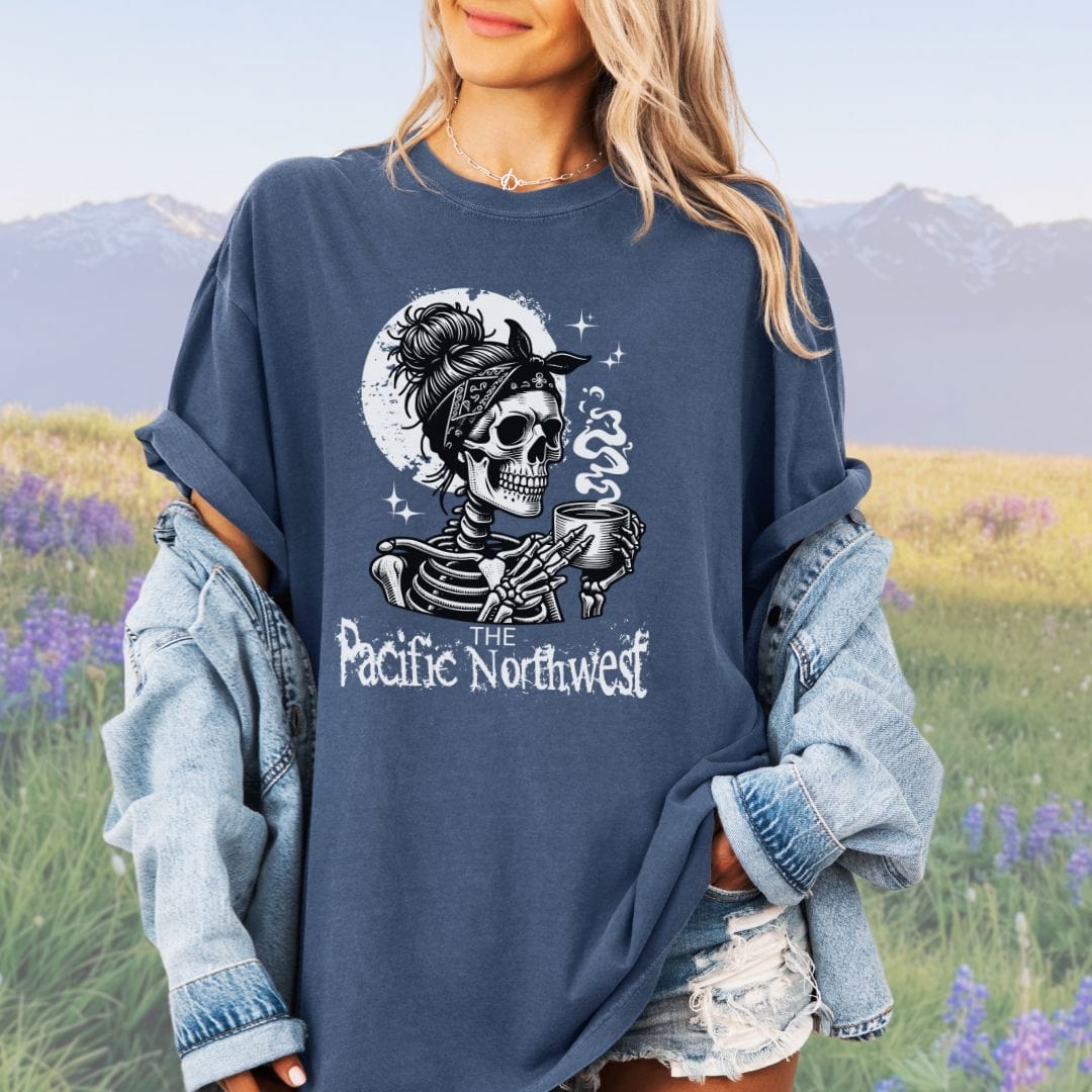 A person wearing a denim colored vintage-style tee with a graphic of a skull holding a mug and the text 'PACIFIC NORTHWEST'.