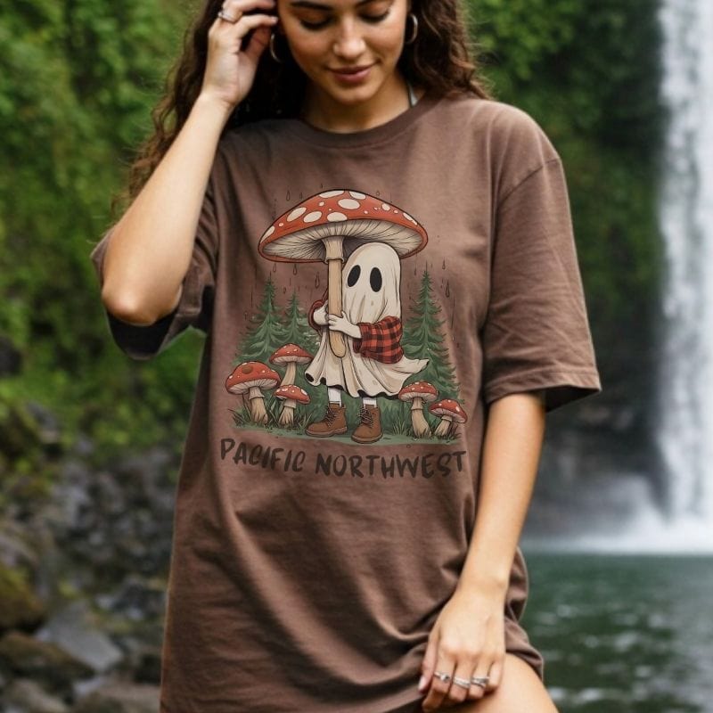 Person wearing a brown t-shirt with a Pacific Northwest design, standing in front of a waterfall.