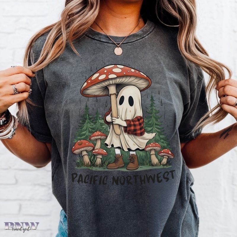 Person wearing a pepper colored, Comfort Colors t-shirt with a ghost and mushroom design, labeled 'Pacific Northwest'.