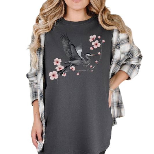 A woman wearing a gray t-shirt with a vintage style and a floral heron design, paired with a plaid shirt and accessorized with a ring.