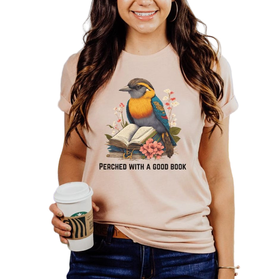 A woman wearing a peach colored  tee with a printed bird and book design.