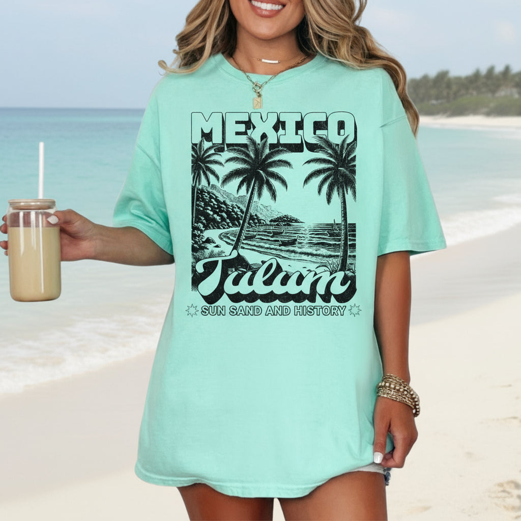 A person wearing a blue green crew neck t-shirt with a vintage-style graphic print of palm trees and the text 'MEXICO Tulum'.