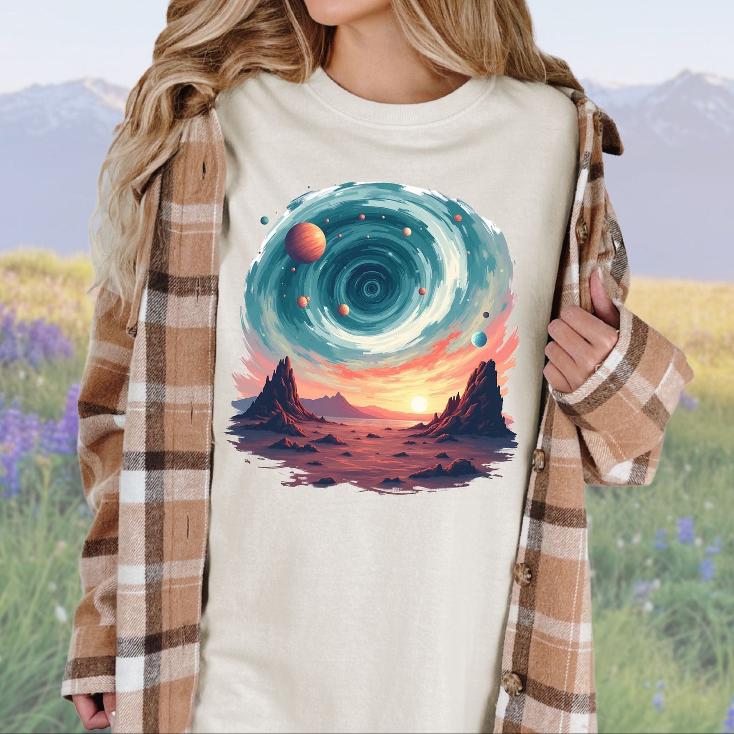 A person wearing a ivory t-shirt with a vintage cosmic swirls graphic, paired with a plaid shirt.