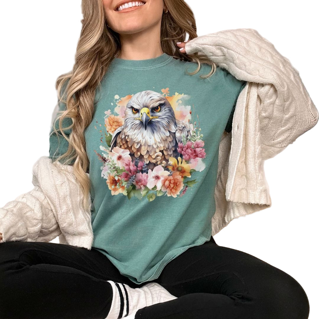 A person wearing a green t-shirt with a floral hawk design, sitting in a cozy bedroom setting.