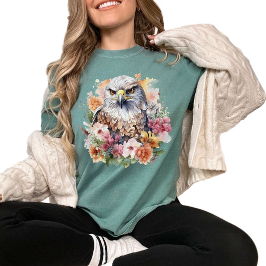 A person wearing a green t-shirt with a floral hawk design, sitting in a cozy bedroom setting.