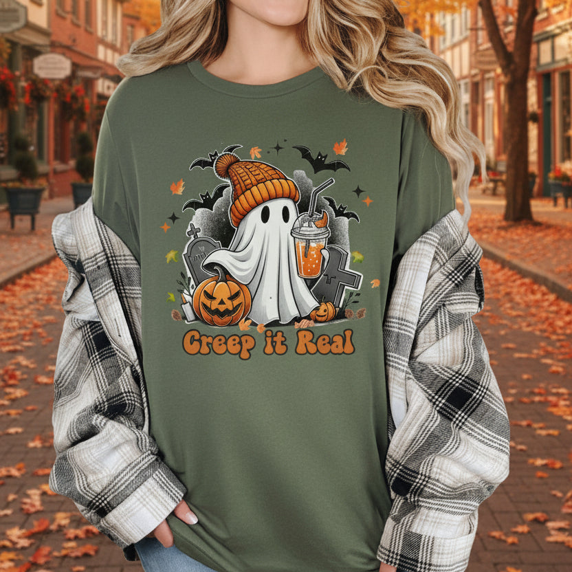 Person wearing a green Halloween-themed shirt with ghost, pumpkins, and text 'Creep it Real' in an outdoor setting with Autumn leaves.