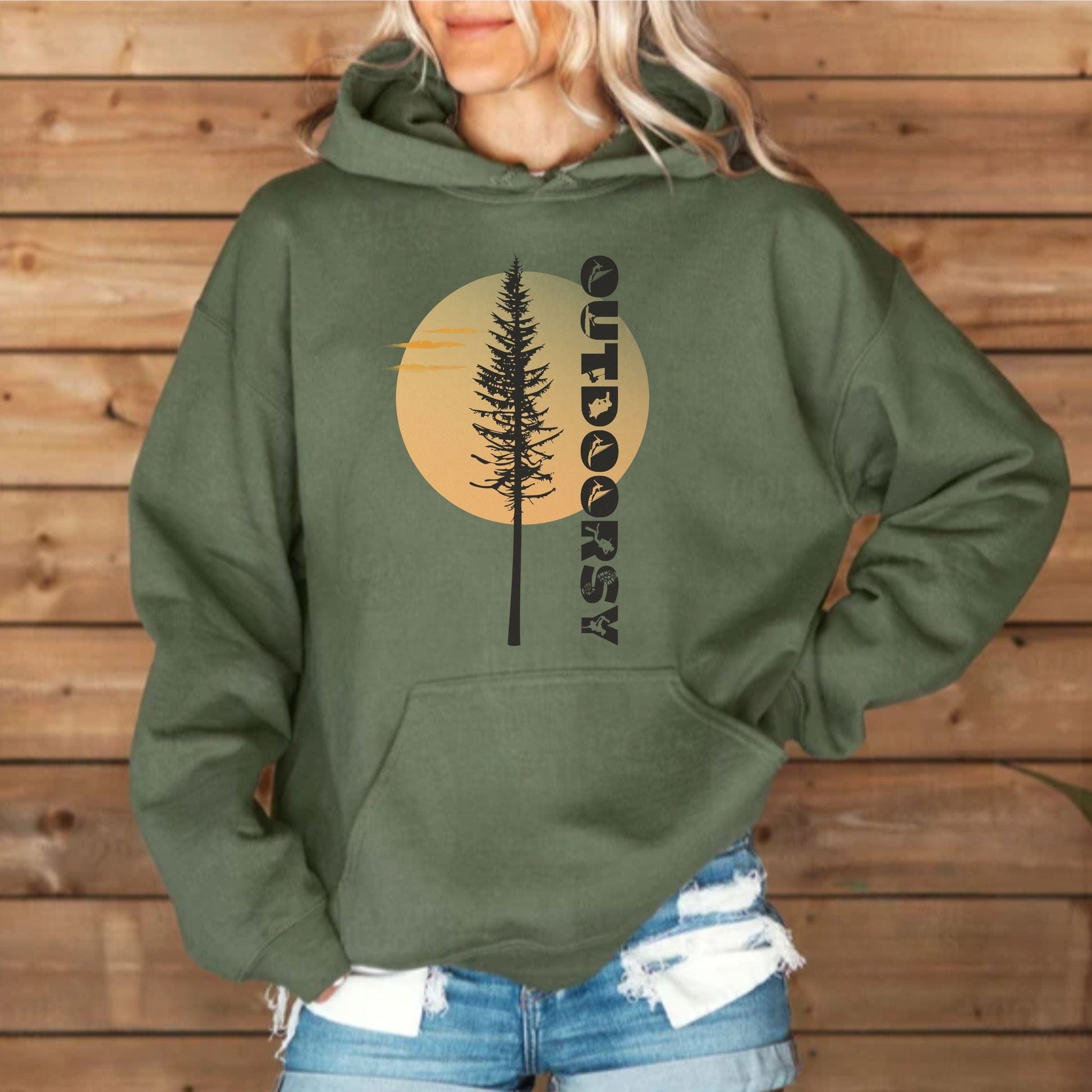 Person wearing a green hoodie with a tree and 'Outdoorsy' design against a wooden background