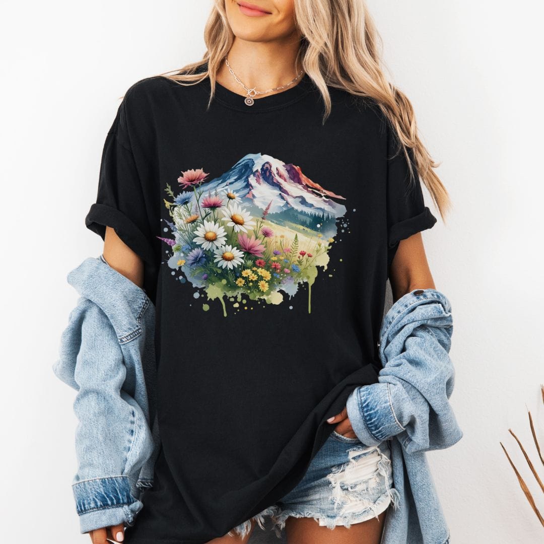 Woman wearing a black Comfort Colors t-shirt featuring a watercolor graphic print of Mount Rainier surrounded by a vibrant meadow of colorful wildflowers and daisies.
