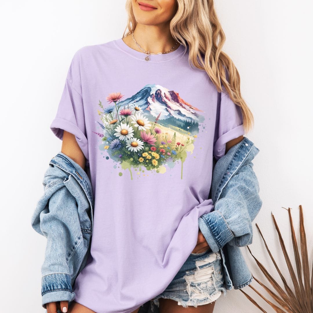 Woman wearing a light purple Comfort Colors t-shirt featuring a watercolor graphic print of Mount Rainier surrounded by a vibrant meadow of colorful wildflowers and daisies.