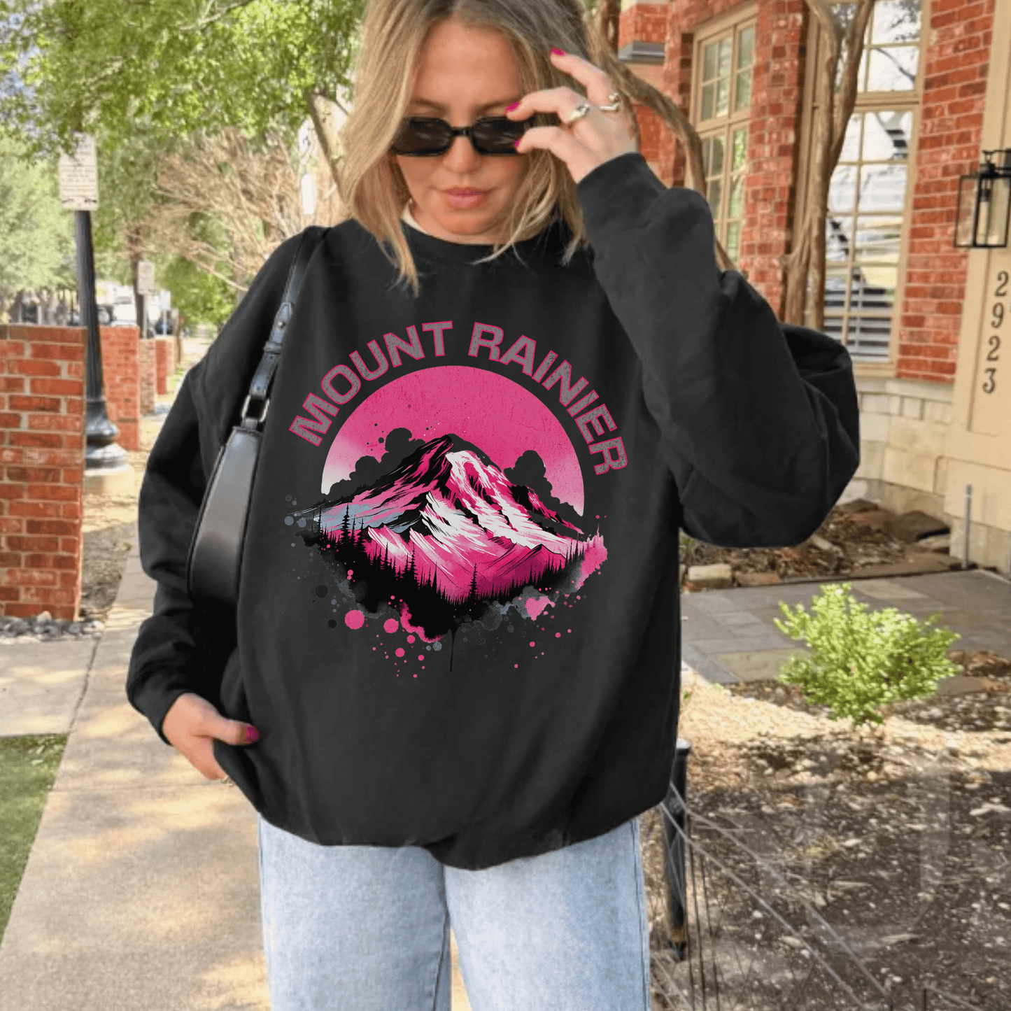 Person wearing a black sweatshirt with Mount Rainier design outdoors.