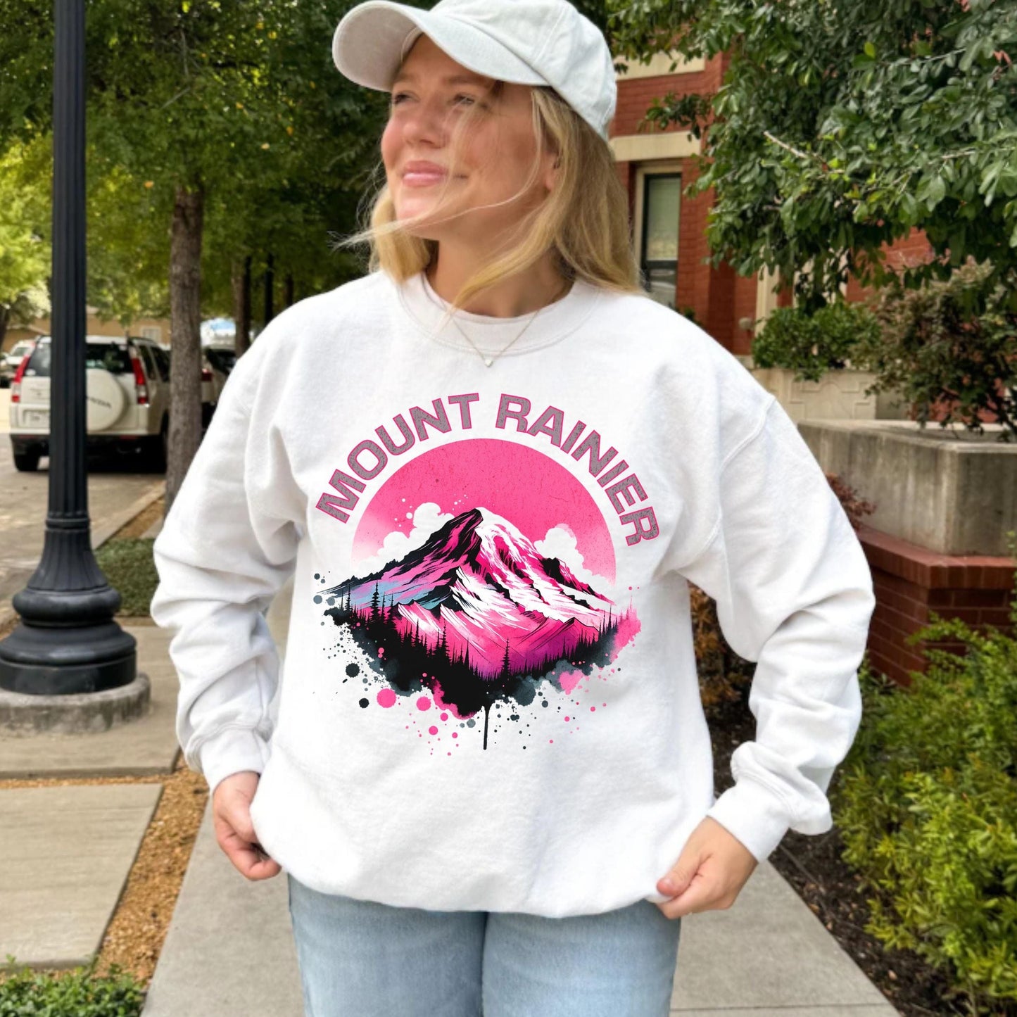Person wearing a white sweatshirt with Mount Rainier design outdoors.
