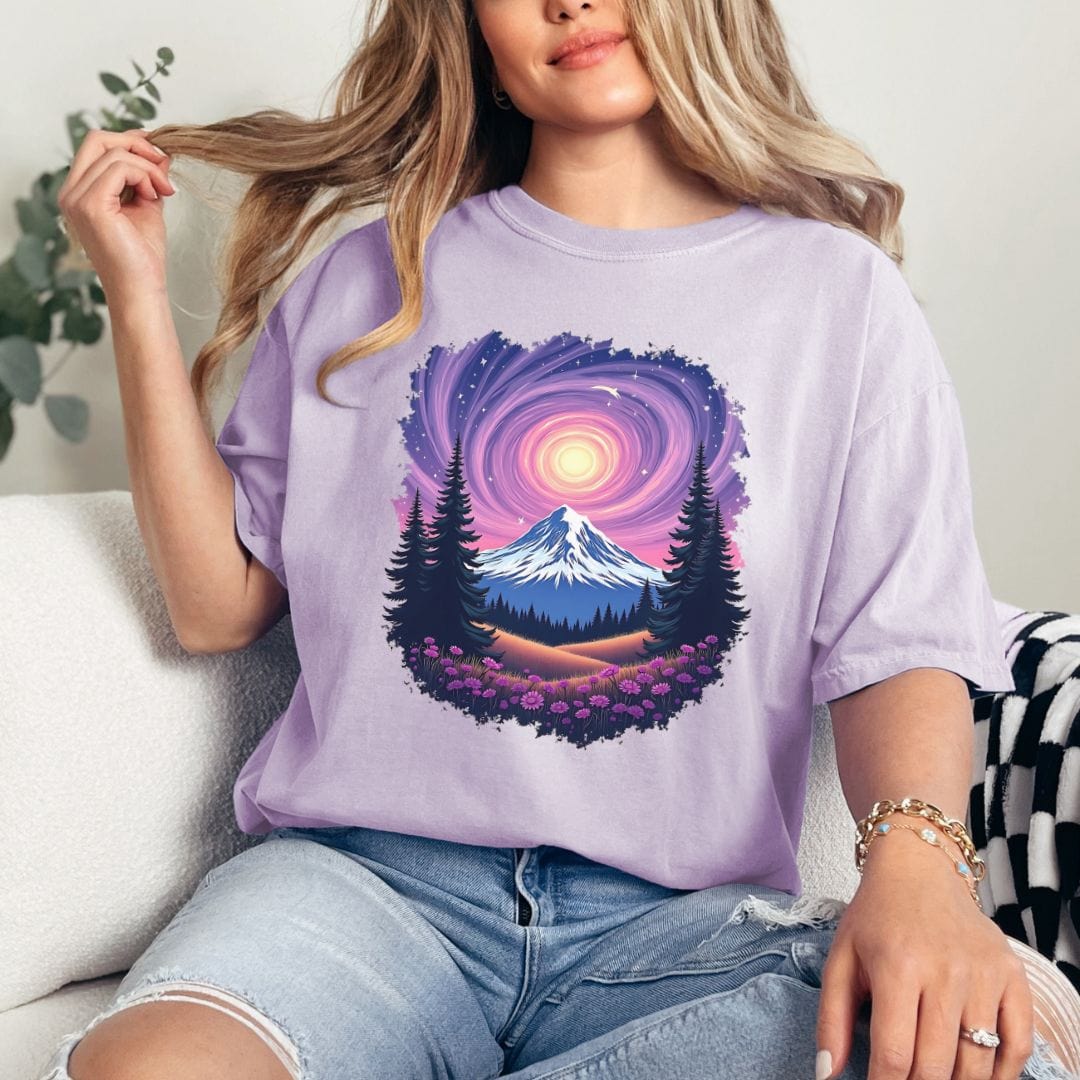 A person sitting and modeling a light purple t-shirt with a vintage-style mountain and starry sky design.