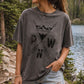 Model wearing a loose, oversized vintage charcoal gray Comfort Colors graphic t-shirt featuring a black, distressed PNW mountain, forest, and arrows design, standing on a wooden dock by a mountain lake