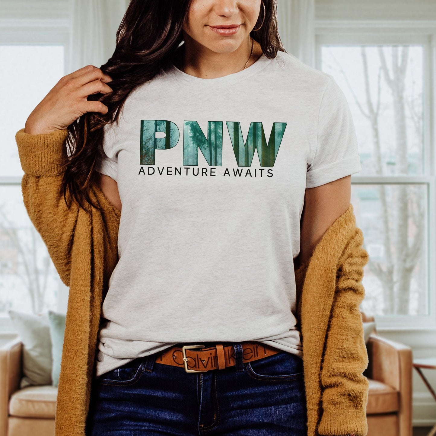 Person wearing a t-shirt with 'PNW Adventure Awaits' text in a home setting