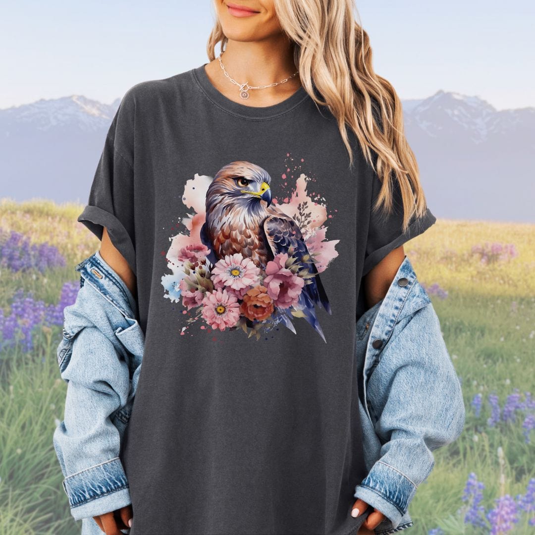 A person wearing a vintage-style pepper colored t-shirt with a graphic print of a bird of prey surrounded by flowers.