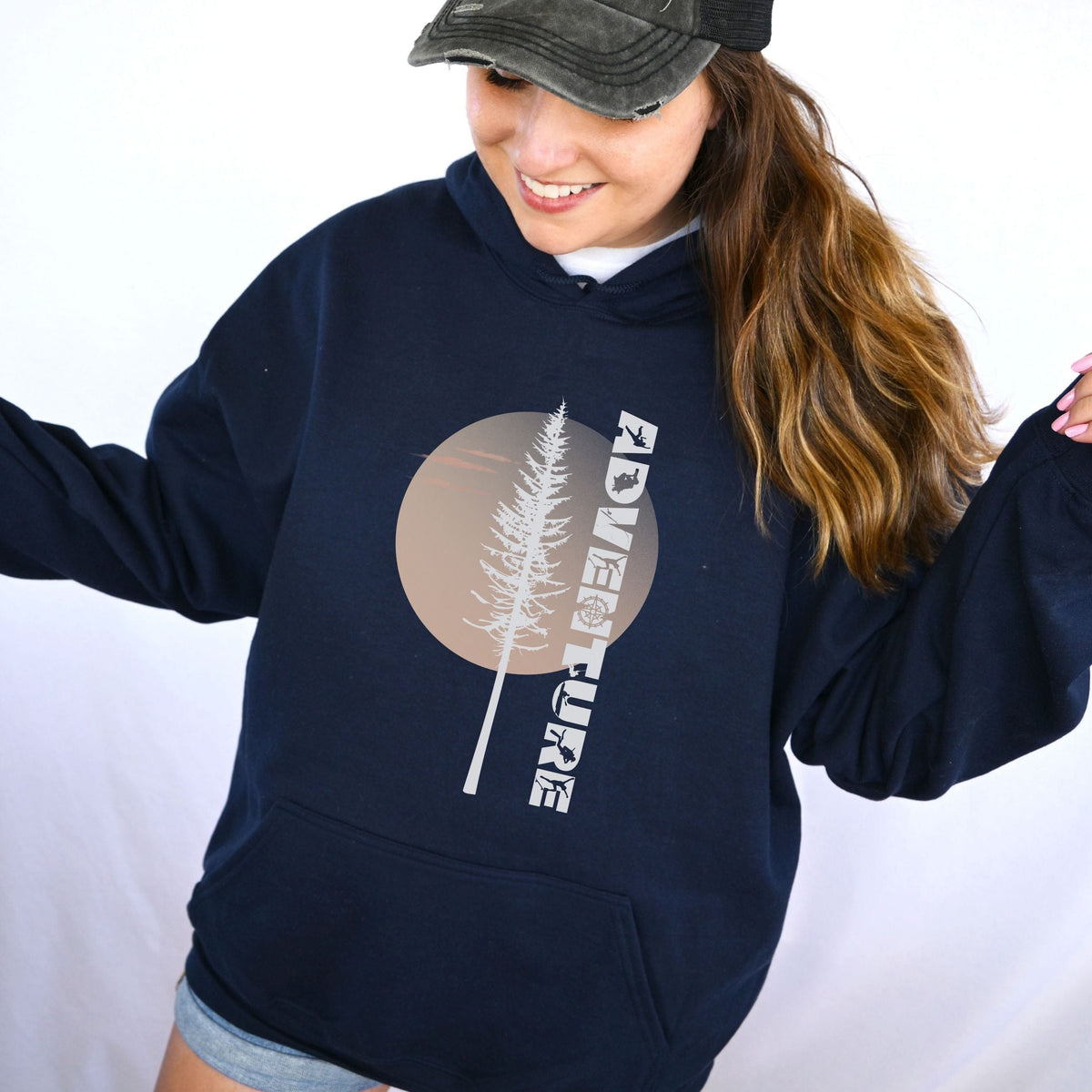 Person wearing a navy hoodie with a tree and 'Adventure' text design on a white background