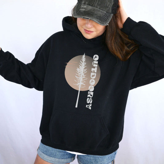 A woman wearing a black pullover hoodie with a circular tree graphic and the word 'OUTDOORSy' printed vertically on the front, paired with denim shorts and a dark baseball cap against a plain white background.
