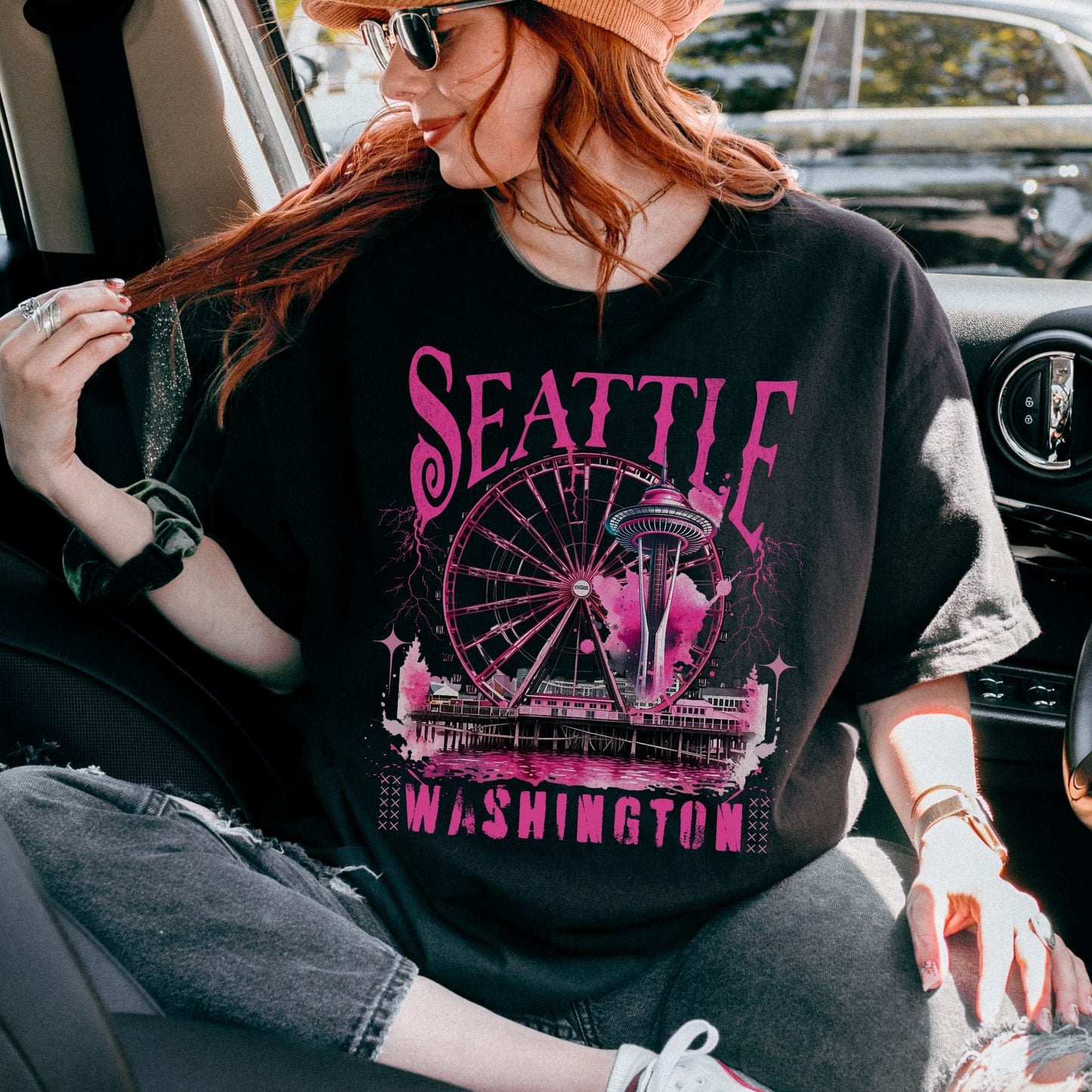 Person wearing a black t-shirt with pink Seattle skyline design, sitting inside a vehicle.
