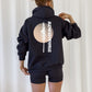 Person wearing a black hoodie with a tree and text design on the back against a white background