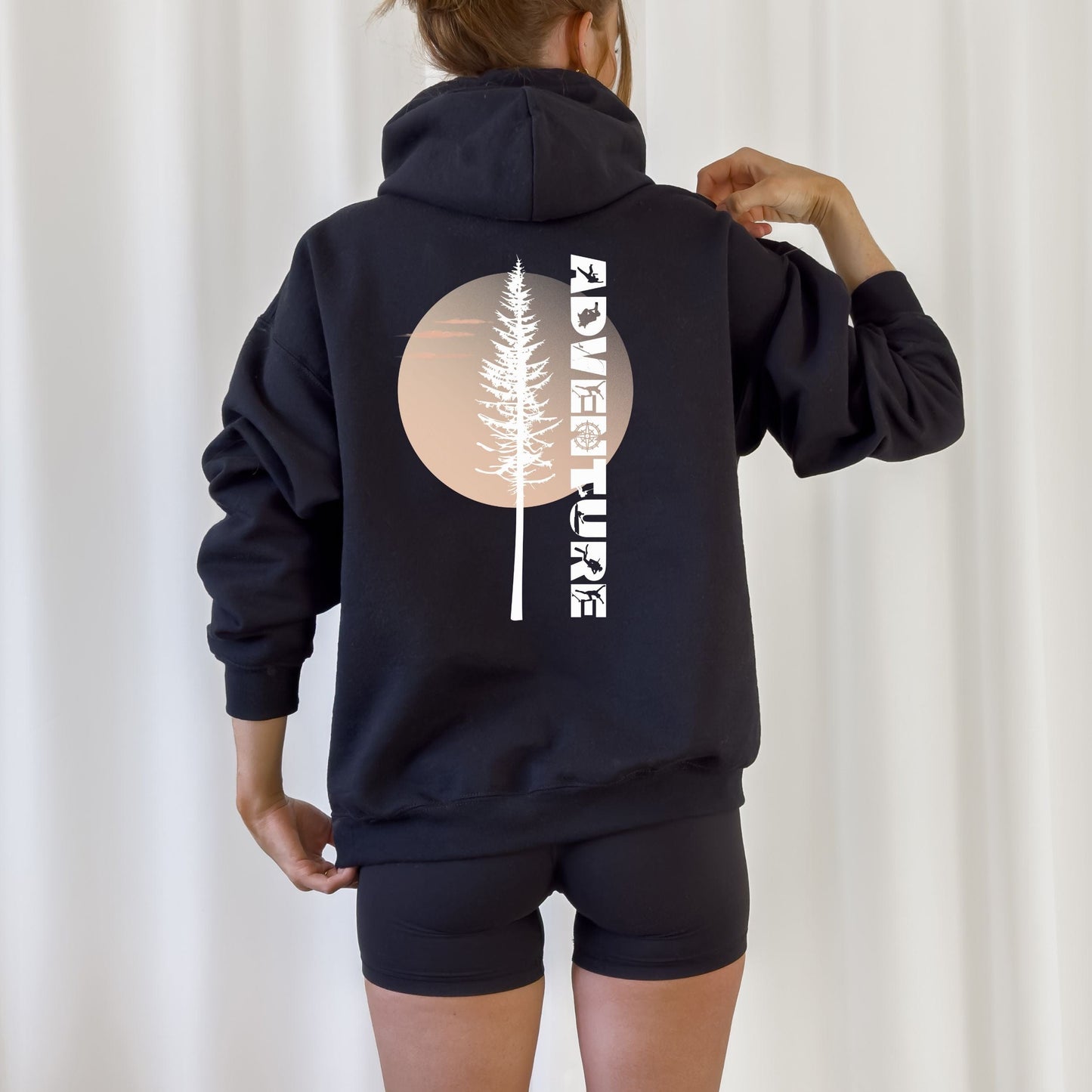 Person wearing a black hoodie with a tree and text design on the back against a white background