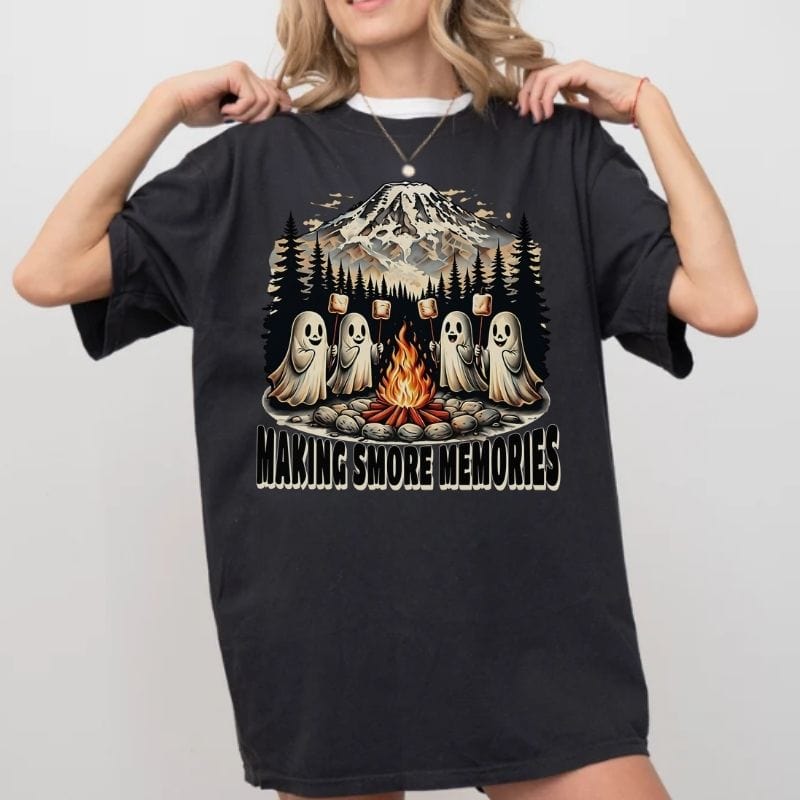Person wearing a black t-shirt with a graphic of ghosts around a campfire and text 'Making Smore Memories' on a plain background.