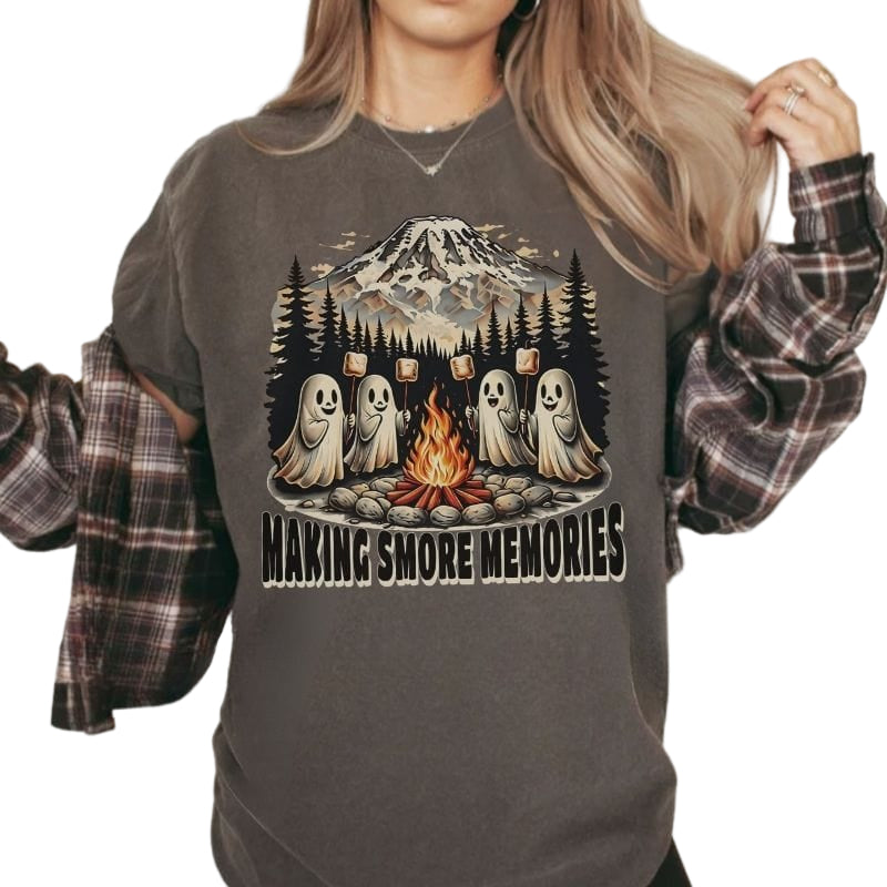 Woman wearing a pepper colored Comfort Colors t-shirt with a vintage illustration of cute ghosts roasting marshmallows by a campfire underneath Mount Rainier Washington.