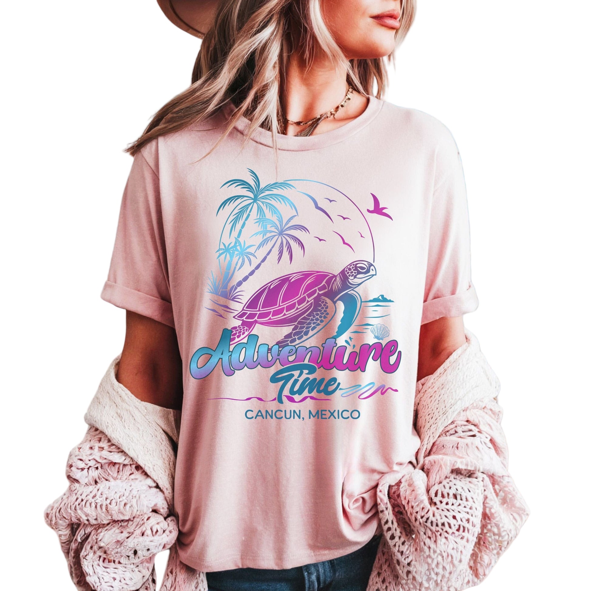 A person wearing a pink t-shirt with a turtle and palm trees graphic, text 'Adventure Time Cancun Mexico', standing on a beach.