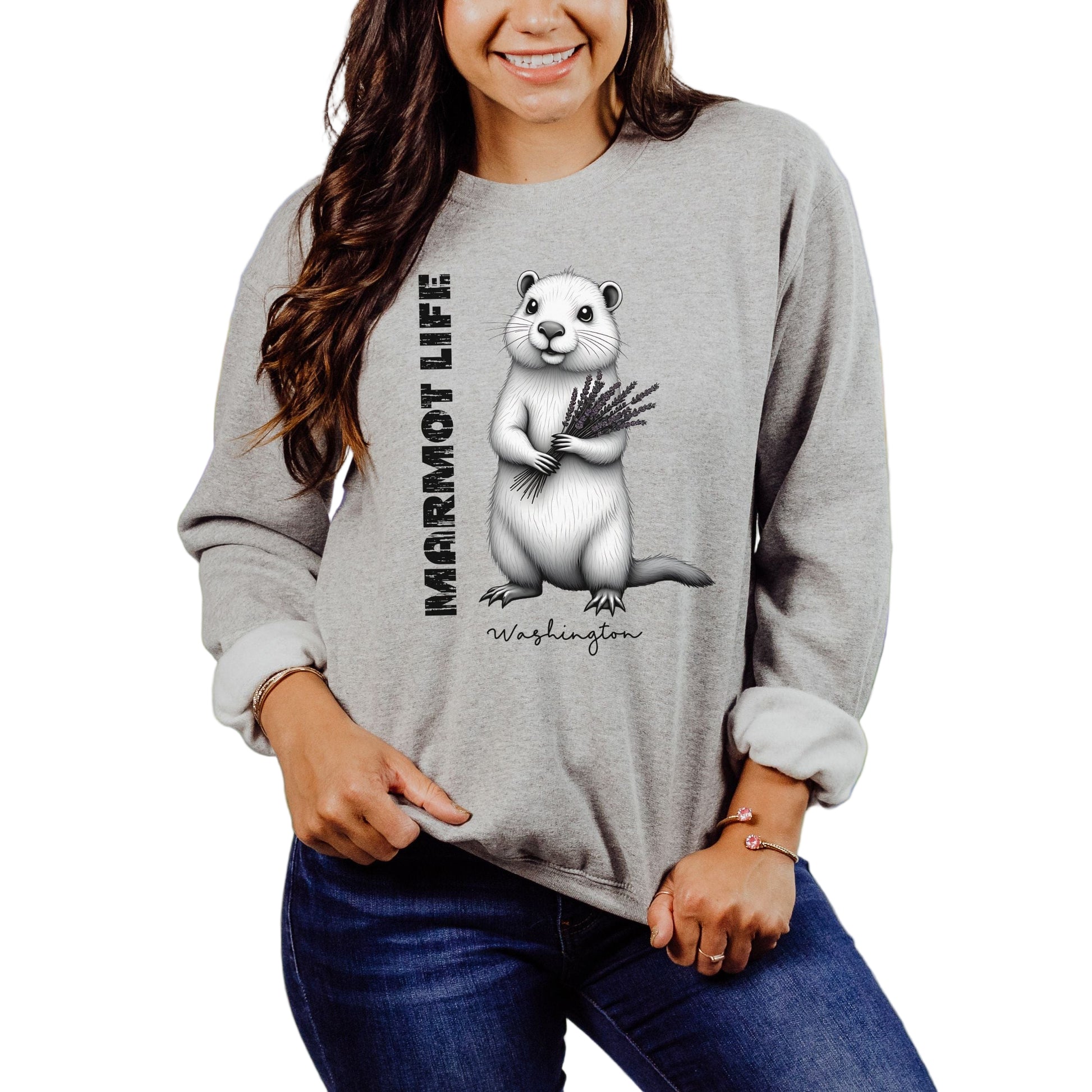 A woman smiling and wearing a gray sweatshirt with a graphic of a marmot holding grass, and the text 'Marmot Life, Washington'. 